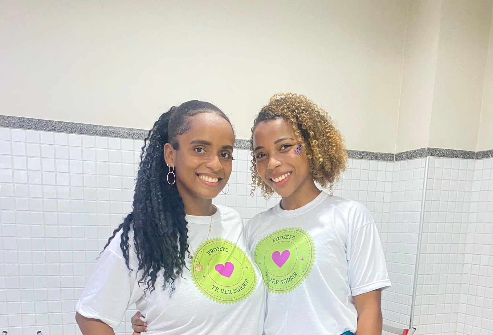 Duas voluntárias sorrindo com a camiseta do projeto